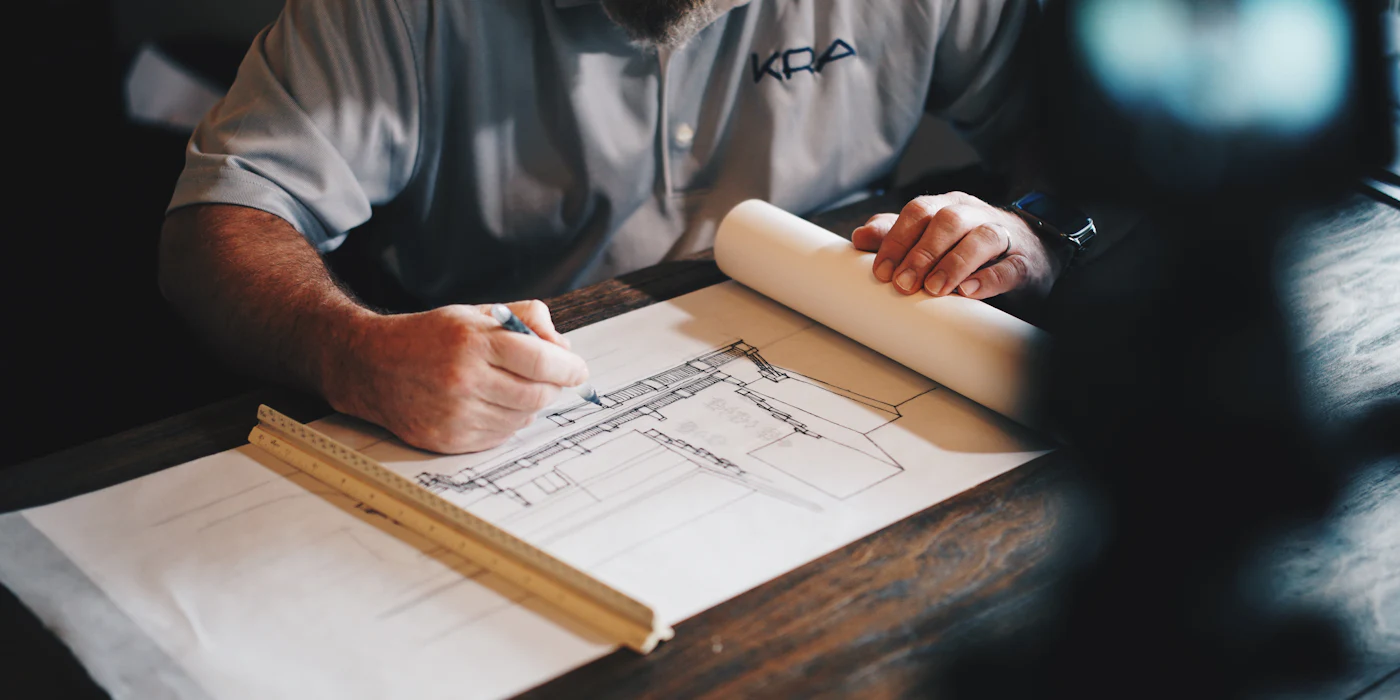 An architect's hands drawing on a technical plan with a pencil and a wooden scale rule